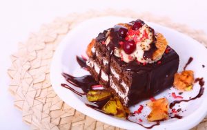 на тарелке лежит кусок шоколадного торта с шоколадной подливой и свежими фруктами